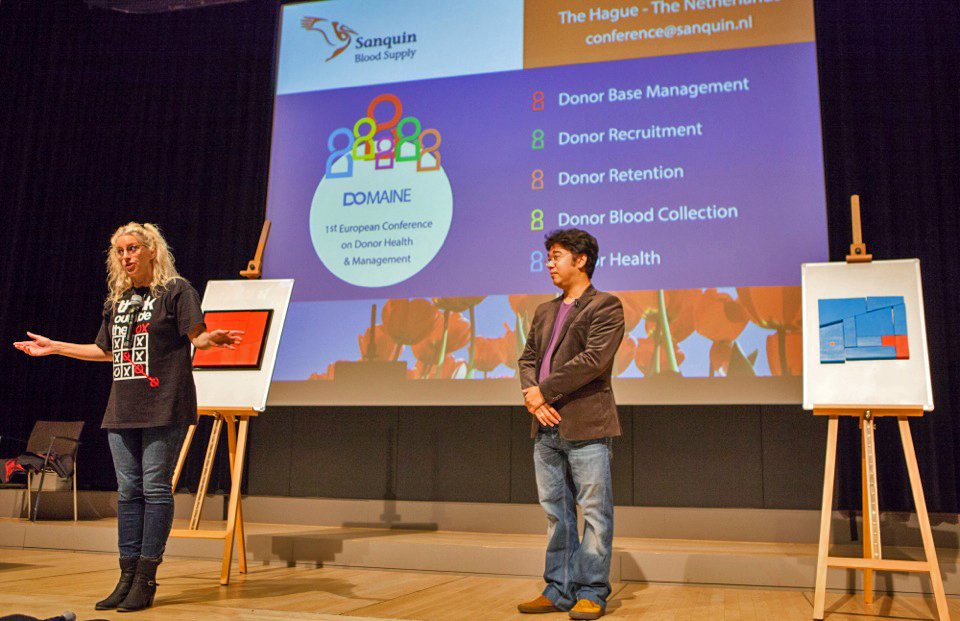 Karin Boon en Dan LeFay op een podium naast twee ezels, voor een scherm tijdens een congres.